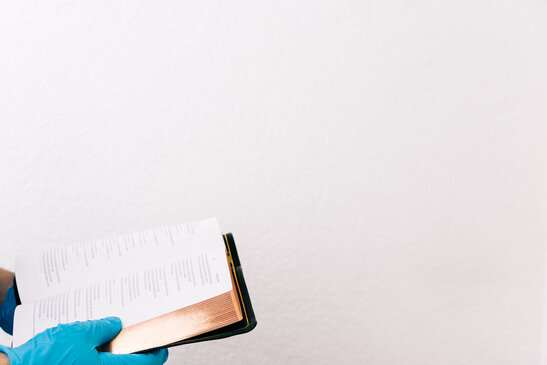 Hands with Gloves on Holding an Open Bible