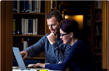 Two people looking at a laptop in a library