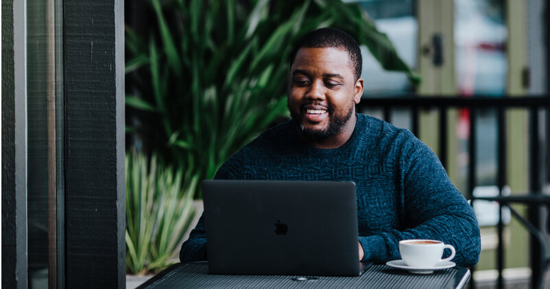 Smiling man using laptop with a cup of coffee