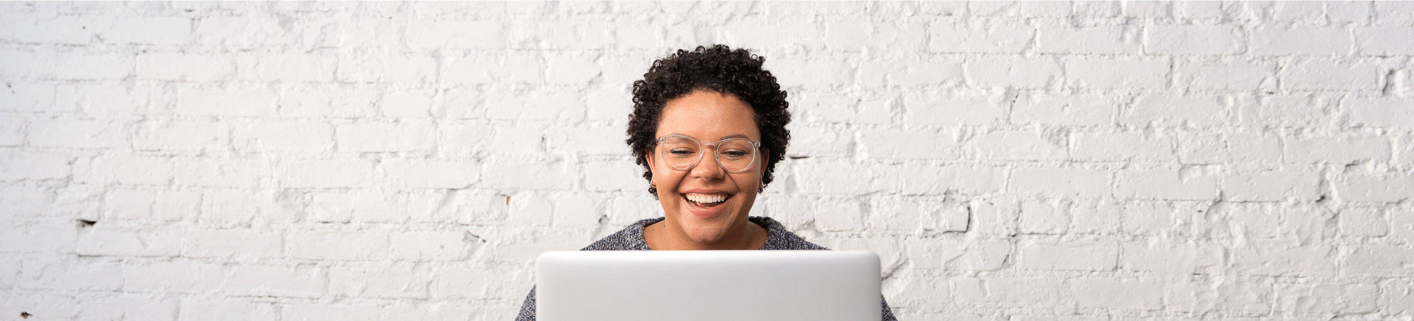 Students sitting at her computer in front of a white painted brick wall