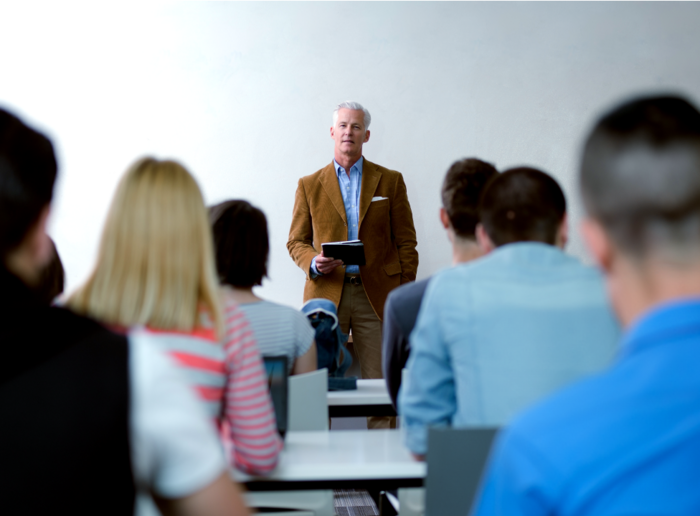 Professor standing in front of class holding a notebook