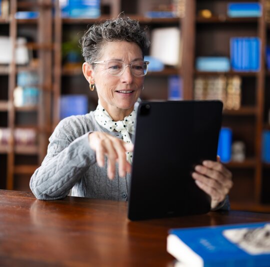 A woman smiling while using a tablet in a library setting.