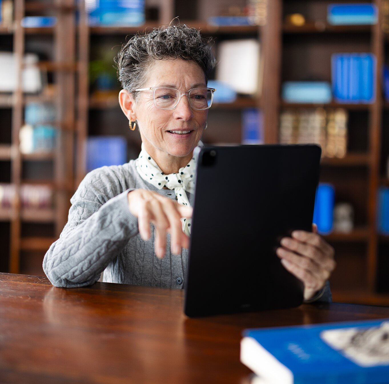 A woman smiling while using a tablet in a library setting.