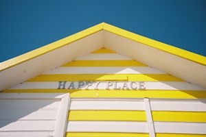 A striped yellow and white English beach hut with the name of "Happy Place". A dark blue sky is in the background. Shot on film.