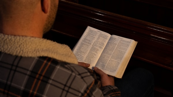 Man reads a bible sat on a wooden church pew. Photograph by Mark Stuckey.