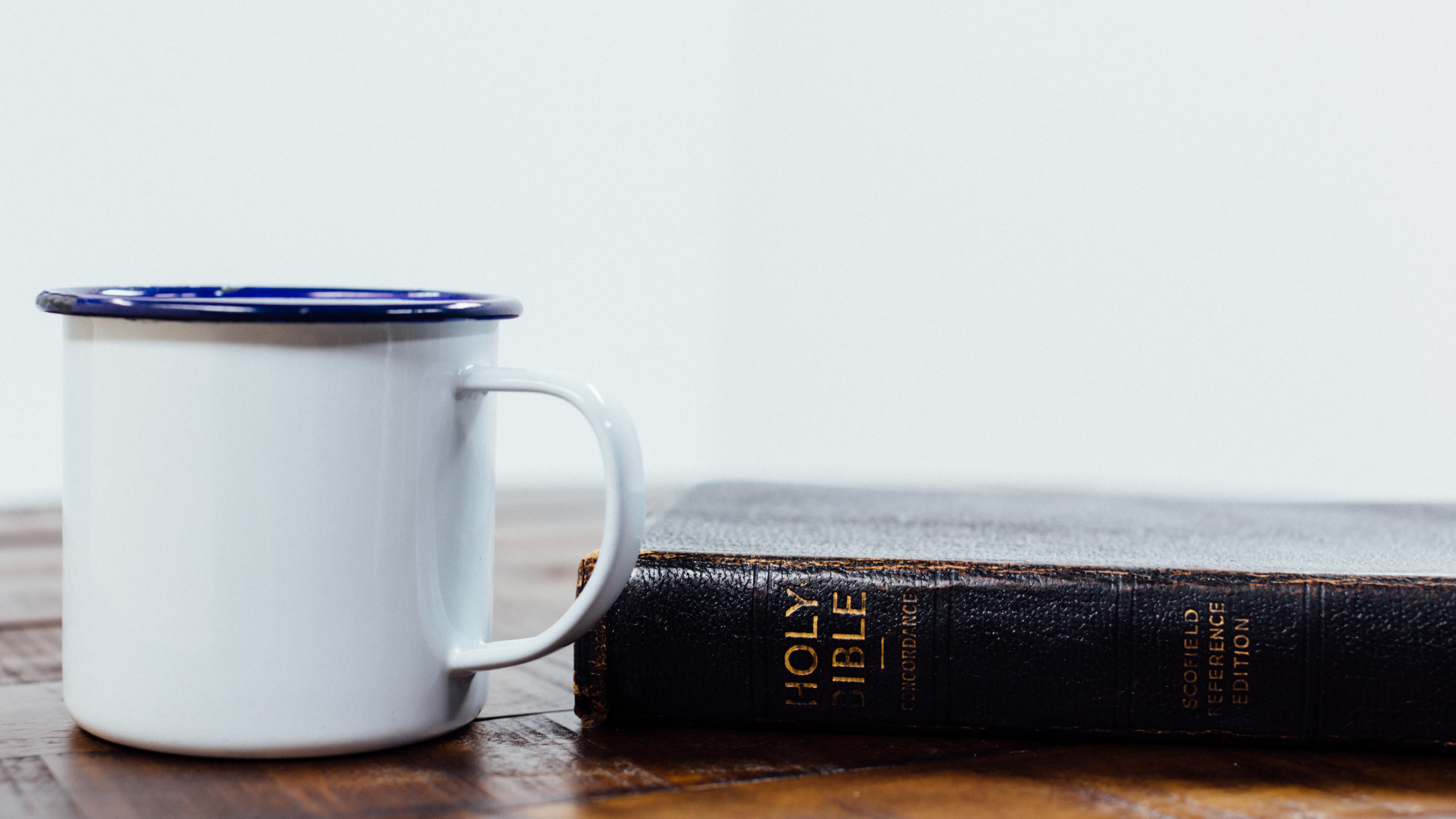 Coffee in mug with bible on wood