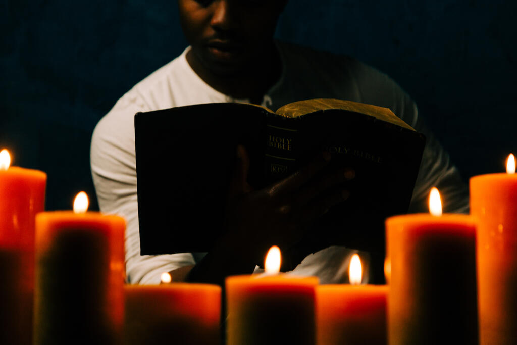 Man Reading Bible in Candle Lit Room large preview