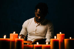 Man Reading Bible in Candle Lit Room  image 4