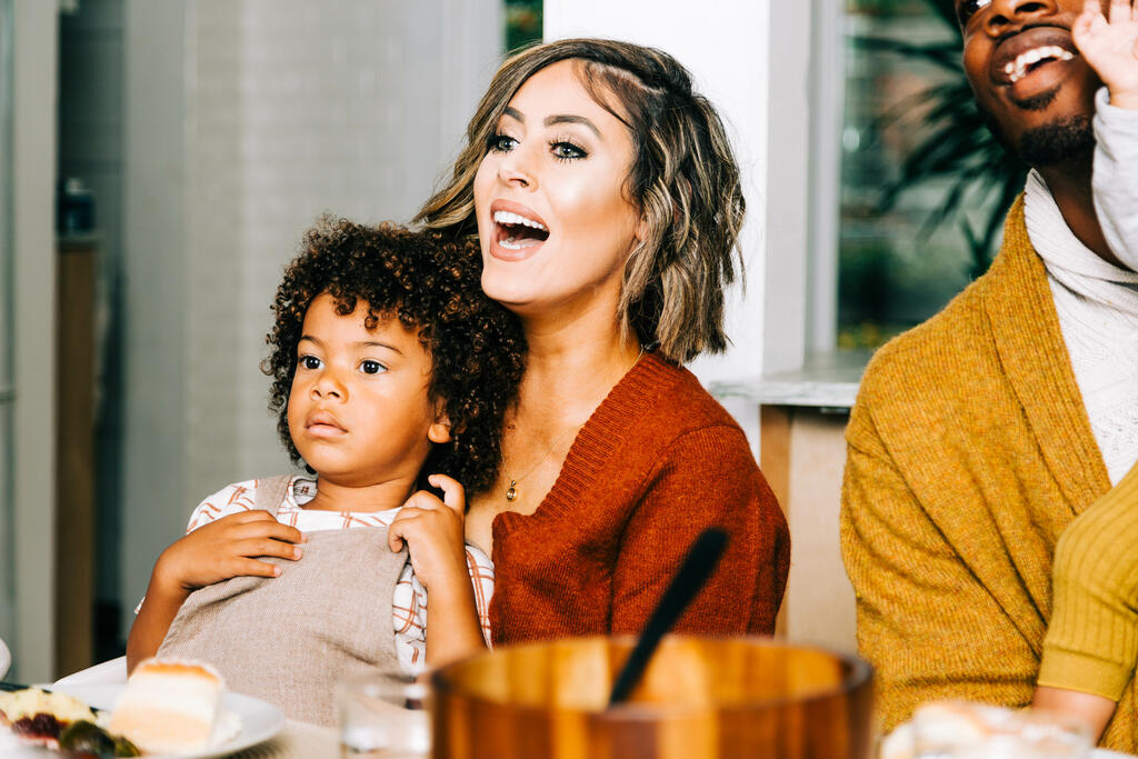 Mother Holding Son in Lap While Laughing with Family at the Thanksgiving Table large preview