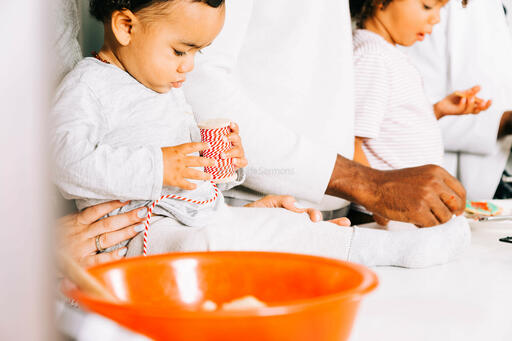 Baby Playing with Red String While Family Bakes in the Kitchen