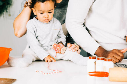 Baby Playing with Red String While Family Bakes in the Kitchen