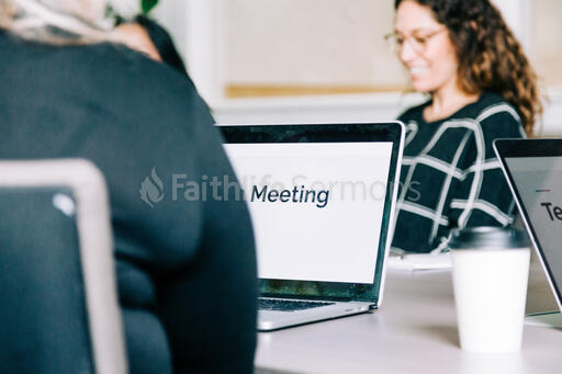 People Seated at Conference Table with Laptops Out for a Meeting