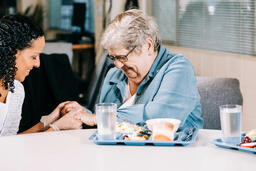 Volunteer Praying with an Elderly Woman at a Community Meal  image 1