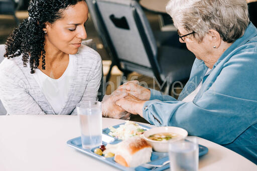 Volunteer Praying with an Elderly Woman at a Community Meal