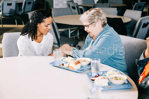 Volunteer Praying with an Elderly Woman at a Community Meal