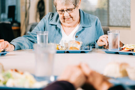 Elderly Woman Praying Before a Community Meal