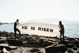 People Holding a He Is Risen Banner at the Beach  image 1