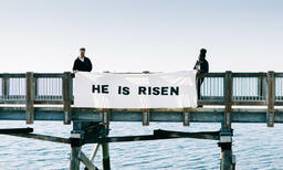 People Holding a He Is Risen Banner over the Side of a Boardwalk  image 2