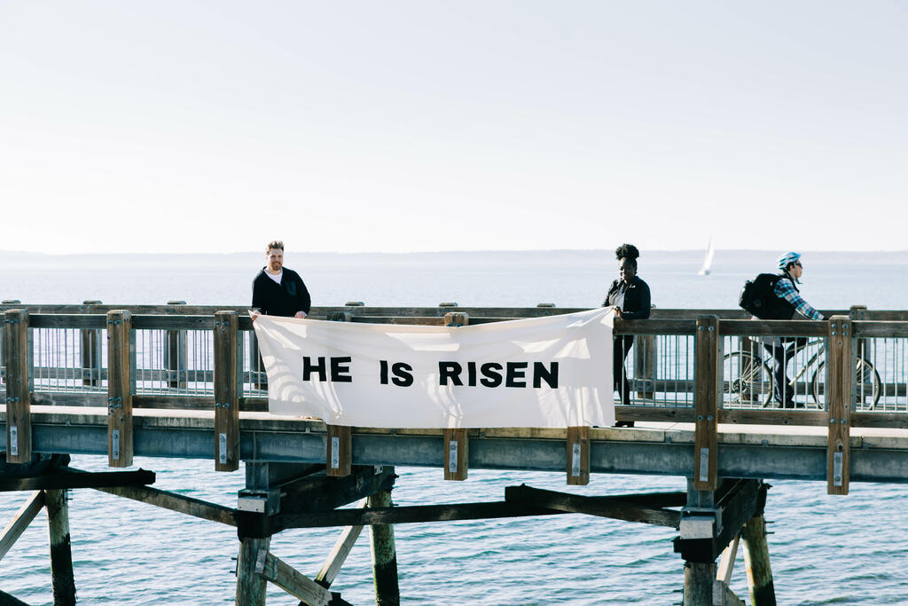 People Holding a He Is Risen Banner over the Side of a Boardwalk large preview