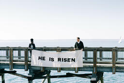 People Holding a He Is Risen Banner over the Side of a Boardwalk  image 3