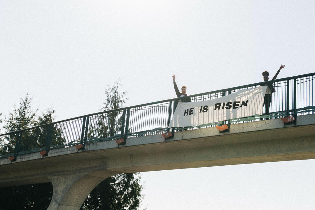 People Holding a He Is Risen Banner Over a Bridge large preview