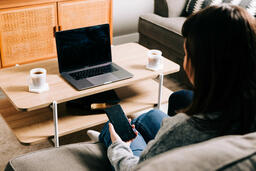 Woman Looking at Her Phone and Watching Church at Home on a Laptop  image 2