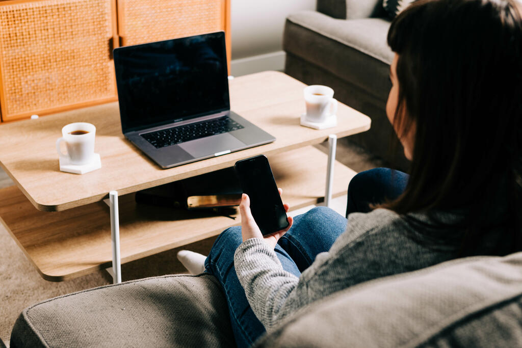 Woman Looking at Her Phone and Watching Church at Home on a Laptop large preview
