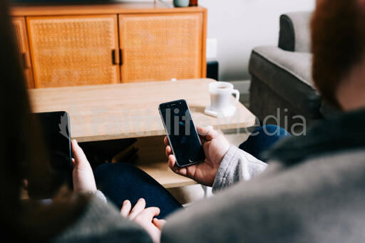 Couple in Living Room Looking at Their Phones in Front of a TV