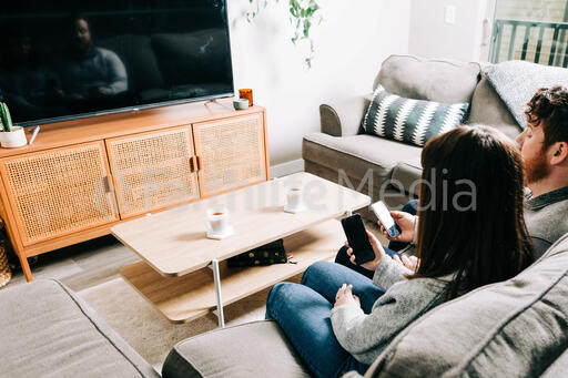 Couple in Living Room Looking at Their Phones in Front of a TV