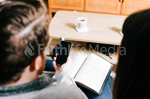 Man Holding His Phone and a Bible