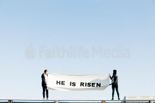 People Holding a He Is Risen Banner on a Rooftop