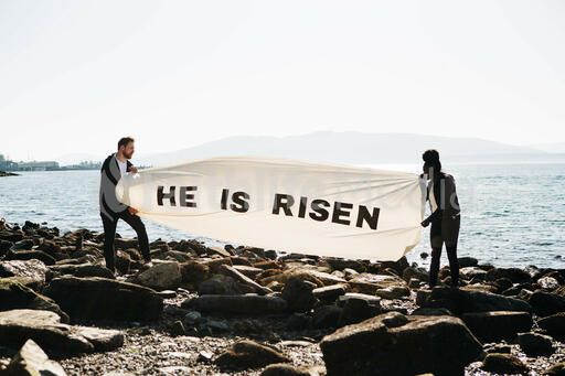 People Holding a He Is Risen Banner at the Beach