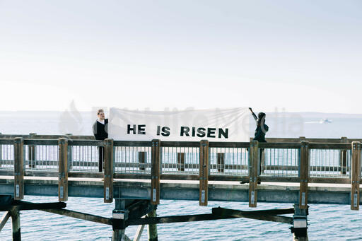 People Holding a He Is Risen Banner on a Boardwalk