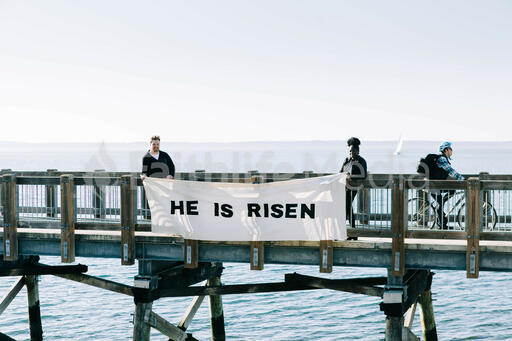 People Holding a He Is Risen Banner over the Side of a Boardwalk