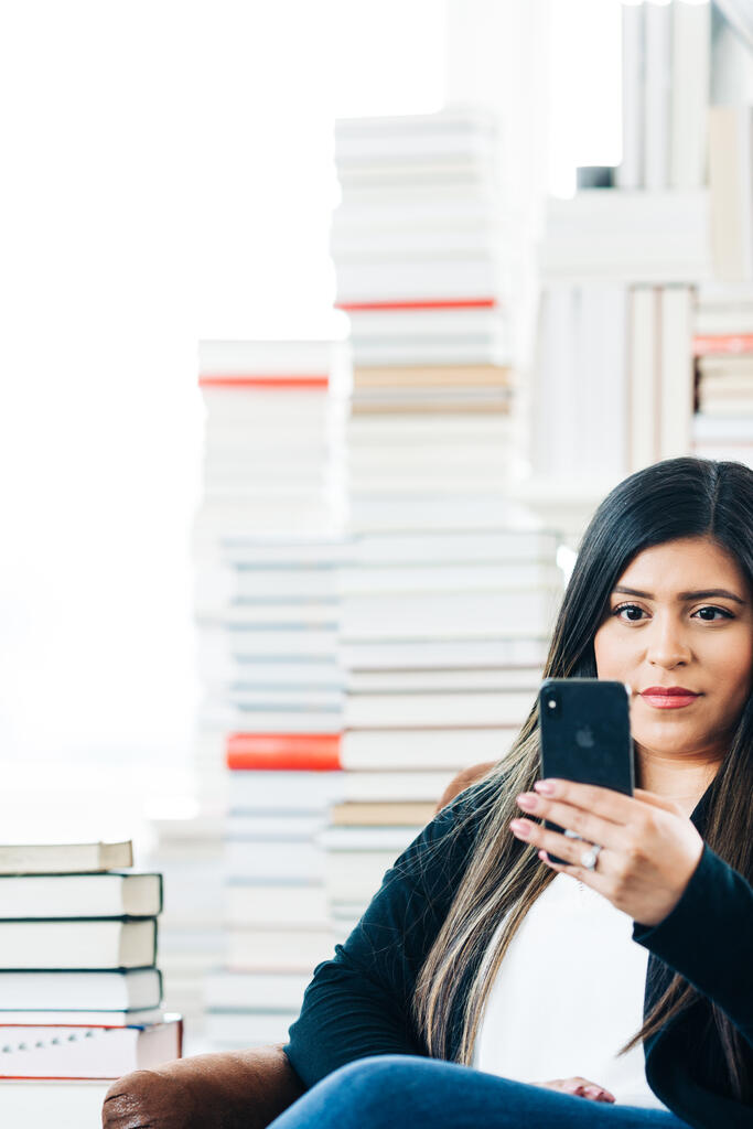 A Woman Studying on an iPhone in a Living Room Full of Books large preview