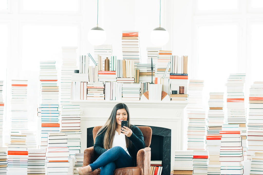 A Woman Studying on an iPhone in a Living Room Full of Books large preview