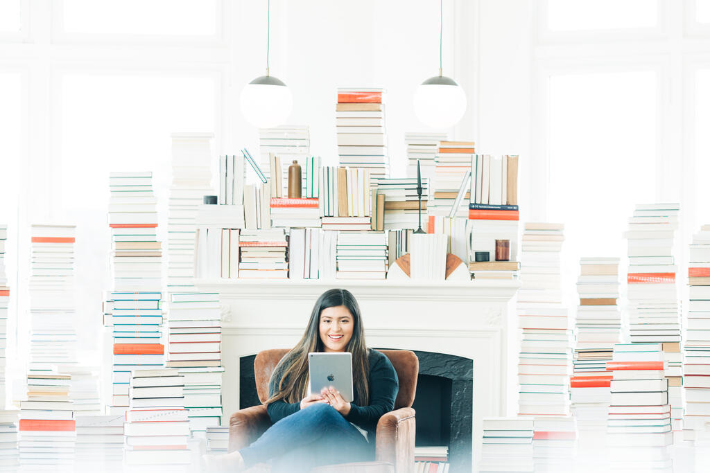 A Woman Studying on an iPad in a Living Room Full of Books large preview