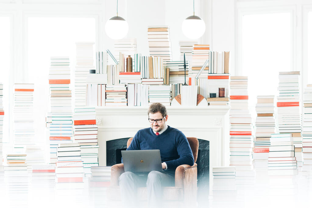 Man Studying on a Laptop in a Living Room Full of Books large preview