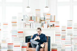 Man Studying on an iPhone in a Living Room Full of Books  image 2