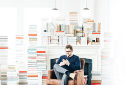 Man Studying on an iPhone in a Living Room Full of Books  image 1