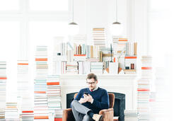 Man Studying on an iPhone in a Living Room Full of Books  image 2