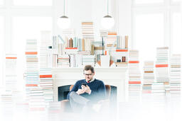 Man Studying on an iPhone in a Living Room Full of Books  image 3