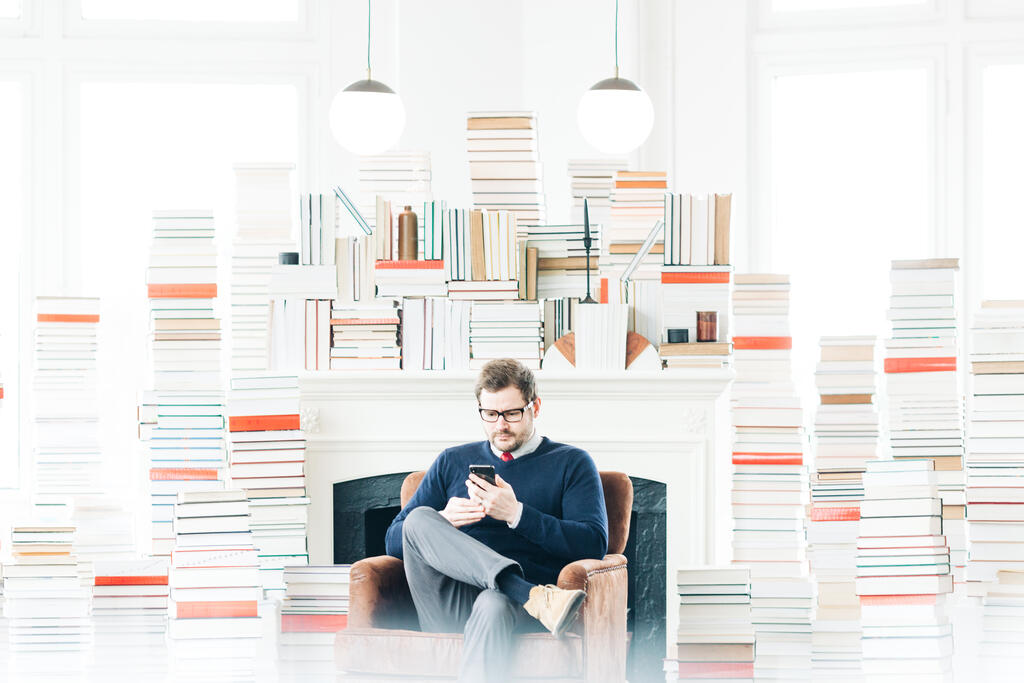 Man Studying on an iPhone in a Living Room Full of Books large preview