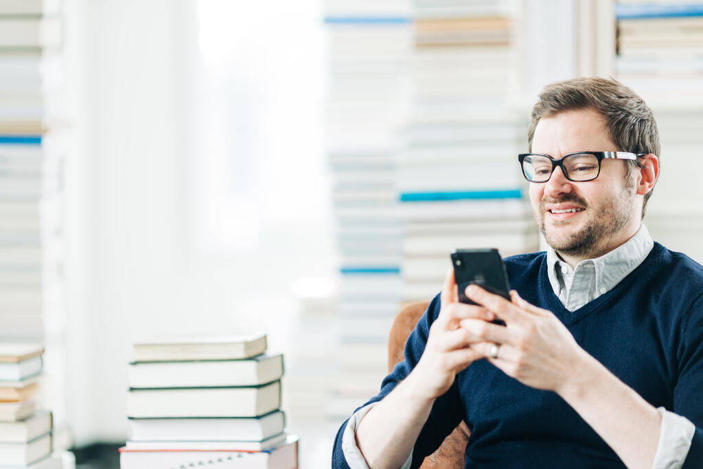 Man Studying on an iPhone in a Living Room Full of Books large preview