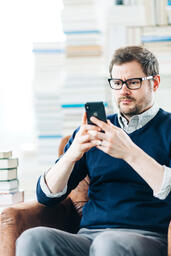 Man Studying on an iPhone in a Living Room Full of Books  image 6