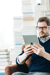 Man Studying on an iPad in a Living Room Full of Books  image 1