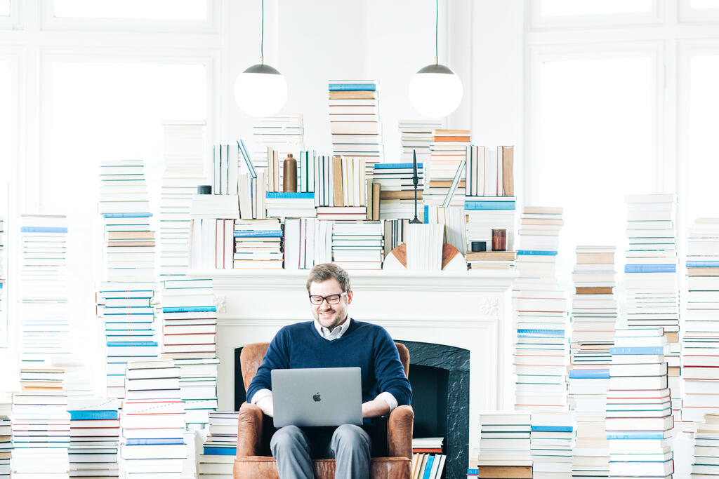 Man Studying on a Laptop in a Living Room Full of Books large preview