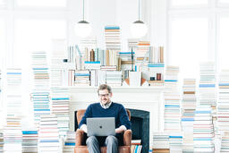 Man Studying on a Laptop in a Living Room Full of Books  image 1