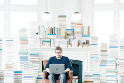 Man Studying on a Laptop in a Living Room Full of Books  image 1