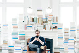 Man Studying on an iPhone in a Living Room Full of Books  image 1